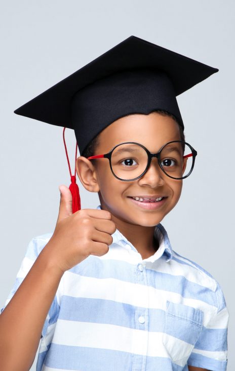 Young African American boy in graduation cap showing thumb up on grey background